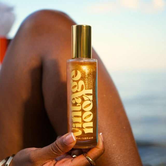 Gilded Sands shimmering body oil held against leg showing golden glow suitable for summer vacation and travel